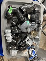Tray filled with various black and grey ABS pipe fittings including elbows, couplings, connectors, and a brass valve fitting on a plastic tray.