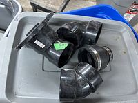 Multiple black ABS pipe fittings including elbow joints, mounting flange, and hose clamp on a gray surface.