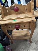 View of wall shelf with two hanging pegs and central red apple knob on natural wood background