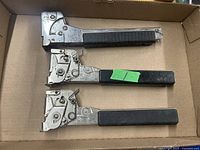 Three heavy duty hammer tackers laid out in a cardboard box, showing metal construction with black handles.