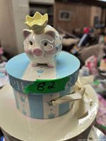 Front view of the ceramic piggy bank showing pig with crown on round pastel-themed lid.