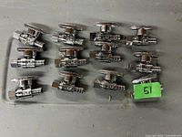 Lot of 12 SharkBite brass stop valves arranged in two rows on a metallic surface with a green label marked '51'.