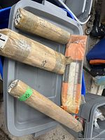 Four packages of arc welding rods on plastic container, one wrapped in orange and black labeled 'Vertex Stainless Steel Electrodes', others wrapped in brown paper with tape, one labeled brass 1/8 diameter.