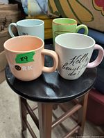 Four colorful mugs arranged on a black round stool showcasing different slogans and colors.