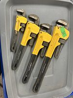 Four yellow-headed Powerfist pipe wrenches laid out in a tray, showing adjustable jaws and serrated grippers.