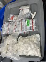 Lot of multiple sealed bags of new white plastic plumbing fittings including tees, elbows, couplings, and connectors on a gray plastic bin.