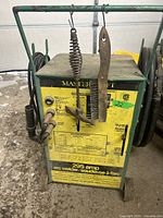 Front view of Mastercraft arc welder showing yellow control panel, model info, and hanging cleaning accessories.