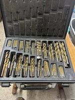 Top view of open black plastic case with Mastercraft logo embossed on inside lid, showing organized drill bits of various sizes with some missing.