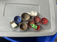 Eight used hole saw cutting tools in various sizes and colors laid out on a gray plastic surface showing signs of rust and paint wear.