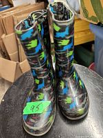 Front view of pair of children's rubber boots with colorful dinosaur print on black background.