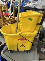 Yellow Rubbermaid mop bucket with wringer and mop handle attached. Bucket shows some dirt and use.