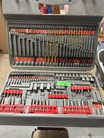 Open carrying case displaying drill bits, screwdriver bits, socket adapters, and driver bits organized in compartments.