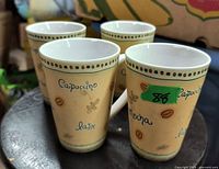 Four ceramic coffee mugs with beige base color and decorative coffee-themed text and coffee bean graphics.
