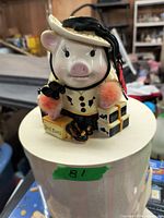 Front view of ceramic piggy bank resembling a pig dressed in hat, black top, and pin with "Shoe Fund" box