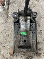 Top-down image of a black metal transmission jack showing the adjustable flat lifting platform with mounting holes, central lifting column, and wheel visible at the bottom.