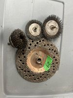 Photo of five used wire wheel brushes of various sizes and types on a white surface. Brushes include large perforated circular, two medium circular with bolt mounts, small round, and cylindrical wire brushes.