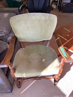 Front view of one green velvet upholstered armchair with wooden frame and button tufting on seat and back.