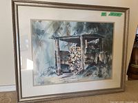 Front angle view of framed watercolor painting of a woodpile stacked in a rustic shelter with a forest backdrop.