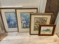 Four framed art pieces leaning against a wall, showing size and framing variety.