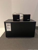 Two small Bose satellite speakers displayed on top of a larger, rectangular Bose Acoustimass subwoofer module with a MaxSold label on the front.