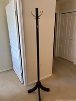 Full view of the tall wooden coat rack standing in a corner, showing the sturdy tripod base and vertical wooden post.
