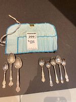 Eight collector spoons displayed on a black surface with a blue cloth holder behind them