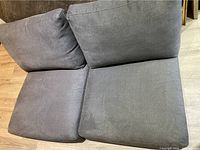 Gray sofa seat cushions and two loose back cushions on wood floor.