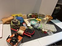 Photo showing assorted fishing gear including Mitchell 758 reel, spinning reel, spools of fishing line, and fishing accessories on table.