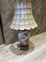 Full view of lamp showing capiz shell scalloped lampshade and ceramic base with cord and plug.