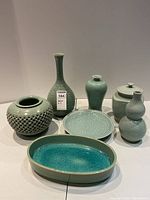 Full set of seven green glazed decorative ceramic pieces arranged on a white surface.