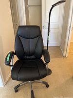 Front view of black office chair with armrests and black floor lamp behind it