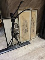 Three framed drawings and a black metal dancing sculpture positioned against a wall on floor