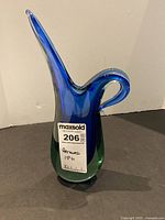 Front view of the blue and green Murano Sommerso glass vase 13 inches high with a curved handle and narrow spout.