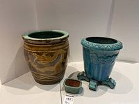 Photo of three plant pots including large brown pot with dragon motif, tall blue pot on stand, and small green rectangular pot with crack.