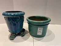Two plant pots side by side: One blue glazed with ornate design and feet, one simpler blue-green glazed pot