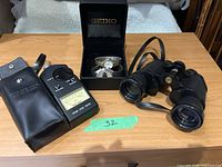 Overview of all components laid out on table: binoculars, sound level meter with case, two wristwatches in Seiko box