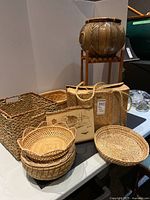 Wide view of all baskets, woolen suitcase, woodburned art, and plant stand with ceramic pot displayed on table