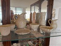 Overview of the set showing larger and smaller pitchers, bowls and plates with consistent embossed basketweave and floral patterns in pale cream color.