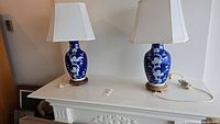 Full view of two blue ceramic table lamps on a white surface, each with a wood base and a white lampshade.