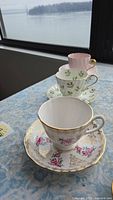 Three assorted teacups and matching saucers on a table near a window with a water view background