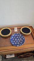 Plate set on wooden surface, showing the six dark cobalt plates with gold edges and single floral patterned plate.