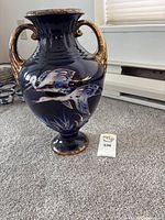Front view of the English pottery vase sitting on carpeted floor showing the bird artwork and gold-accented handles.