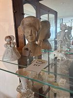 Photo showing bust of woman in headdress, lady in traditional dress, and smaller figurines on glass shelf