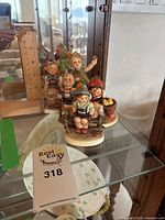 Display of six Hummel figurines grouped together on a glass shelf, showing details and size relation, with a ruler measuring the height.