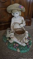 Full view of plaster girl holding basket with ducks on floral grass base