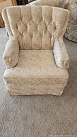 Front view of a cream-colored upholstered armchair with button tufted back and floral pattern.