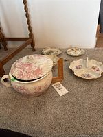 Large lidded tureen with pink floral pattern, two divided serving plates, one small divided plate with handle, and three decorative plates shown together on carpet.