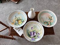 Photo showing all three decorative plates and the miniature Wedgwood vase arranged on a wooden surface