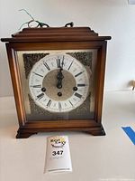 Full view of wooden mantle clock with glass front showing clock face and wood casing.