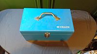 Closed blue metal carry case with handle and Crain logo on lid